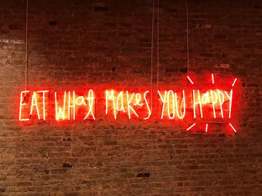 Red neon sign on a brick wall reading "eat what makes you happy"