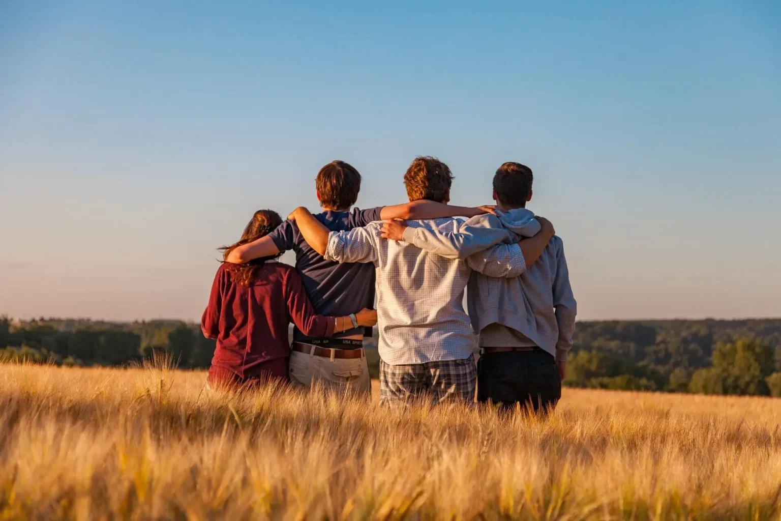 Four people standing in a field with their arms around each other