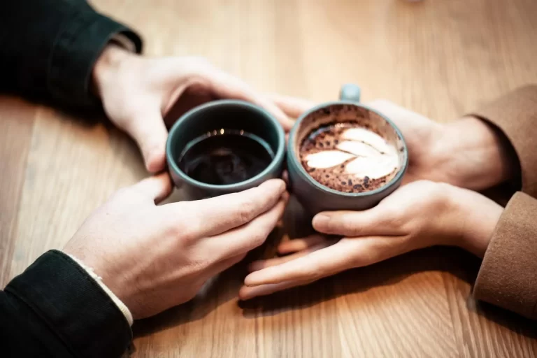 Two people's hands touching and each holding a warm drink