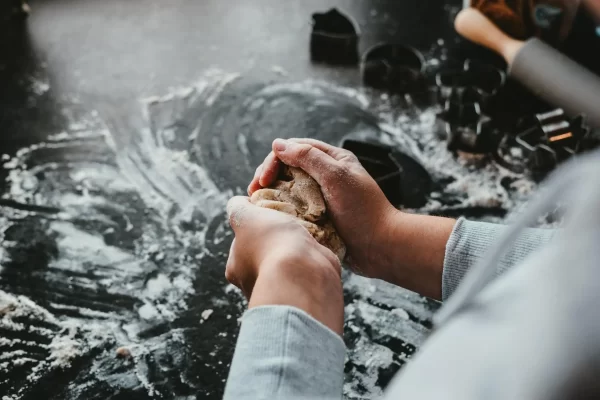 A person holding dough over a counter dusted with flour