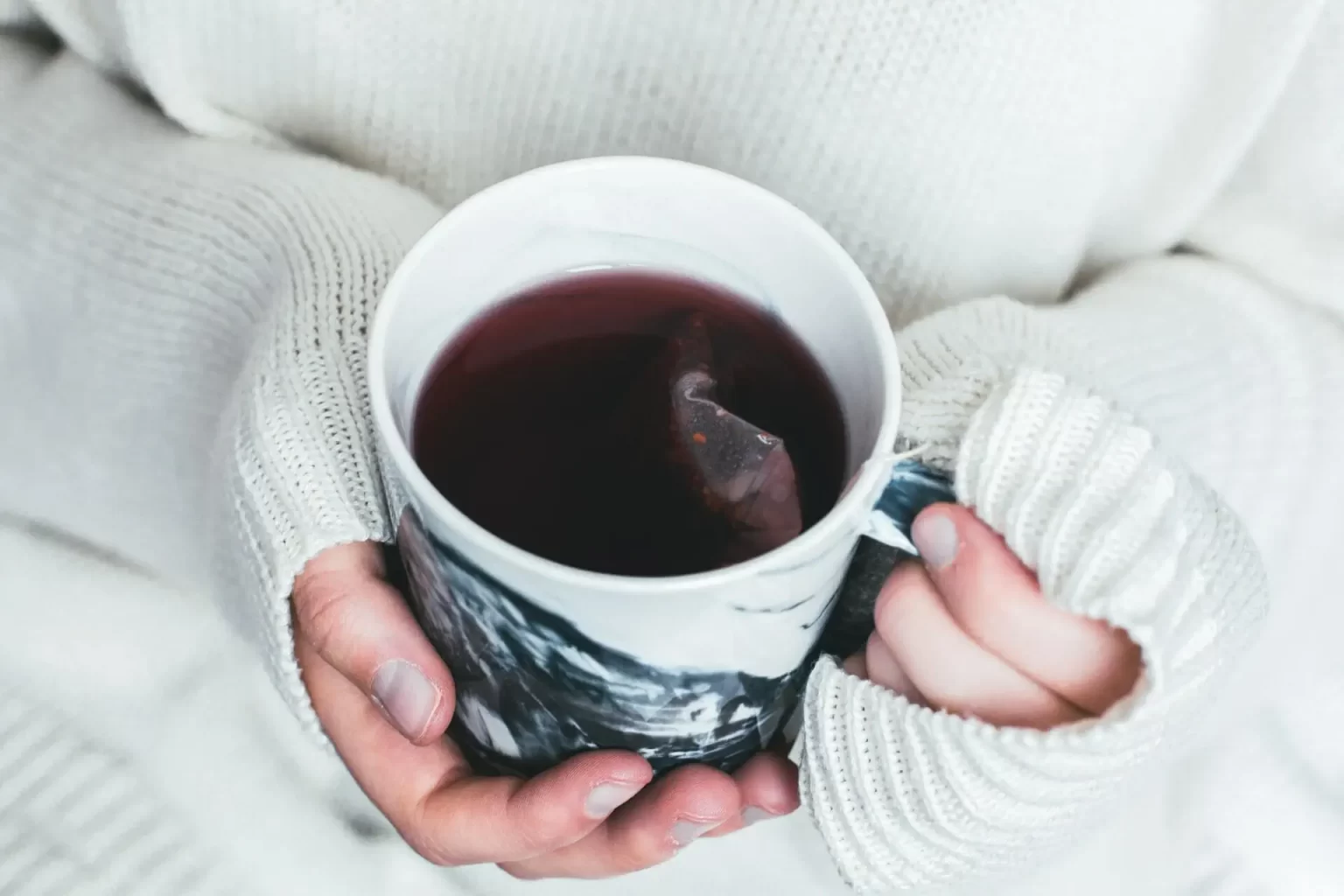 A person holding a cup of tea, wearing a sweater